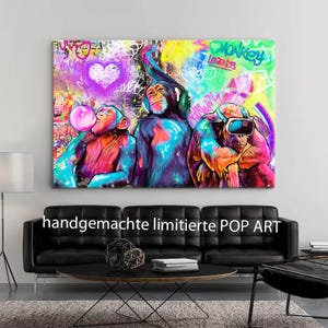Peut inclure: Une toile murale rectangulaire représentant une peinture de style graffiti vibrante de trois chimpanzés. Le singe de gauche souffle une bulle rose, celui du centre porte un casque audio et celui de droite porte des lunettes de réalité virtuelle, sur un fond coloré avec un cœur et du texte.