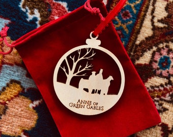 May include: A wooden Christmas ornament with a silhouette of a horse-drawn carriage and a tree. The ornament is red and white and says "Anne of Green Gables".