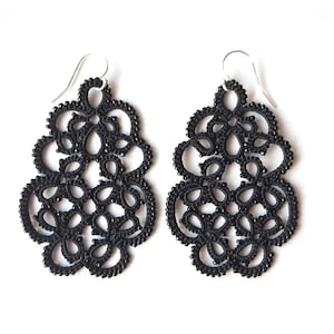 May include: A pair of black dangle earrings with a delicate, intricate design. The earrings are made of black thread and beads, and they have a floral pattern.