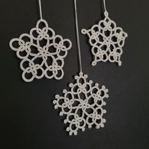 May include: Three white crocheted snowflakes hanging from white string against a black background.