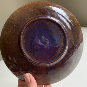 Puede incluir: Un plato de cer&aacute;mica marr&oacute;n con un esmalte azul y morado en el interior. El plato tiene un borde ligeramente elevado.