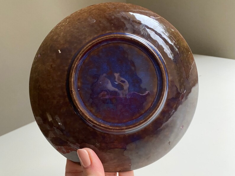 Puede incluir: Un plato de cer&aacute;mica marr&oacute;n con un esmalte azul y morado en el interior. El plato tiene un borde ligeramente elevado.