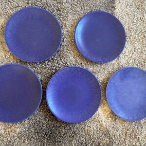 May include: Five blue ceramic plates with a textured surface. The plates are arranged in a semi-circle on a fluffy white surface.