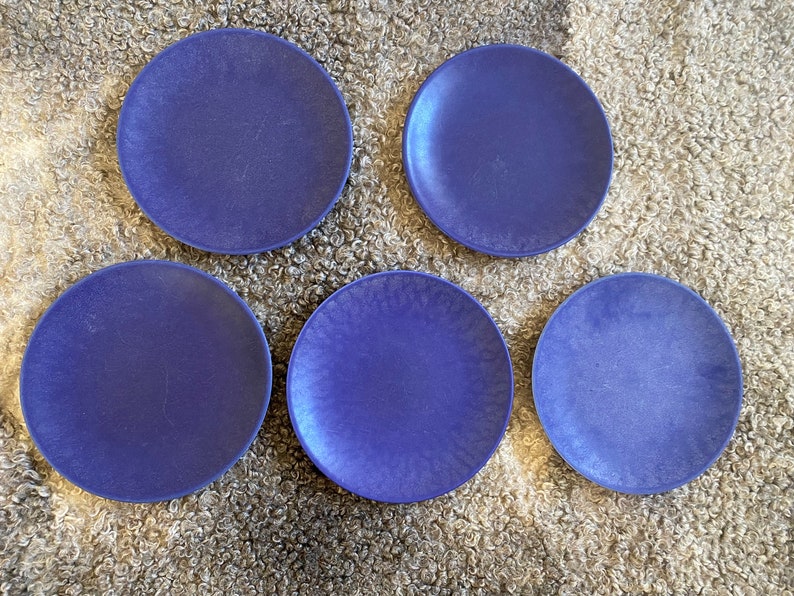 May include: Five blue ceramic plates with a textured surface. The plates are arranged in a semi-circle on a fluffy white surface.