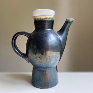 May include: A dark blue ceramic teapot with a white lid and a green glaze. The teapot has a rounded body and a spout on the side. The base of the teapot is a darker blue.