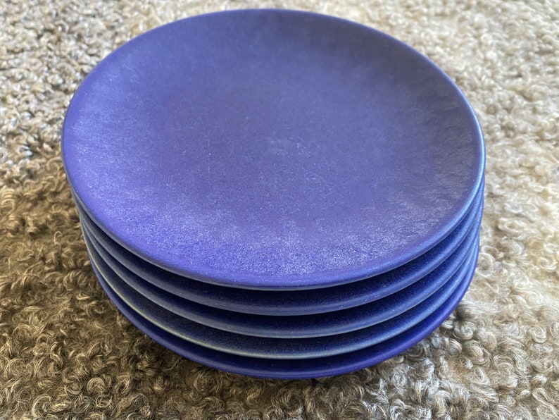 May include: A stack of five blue ceramic plates. The plates are a deep blue colour and have a slightly textured surface.