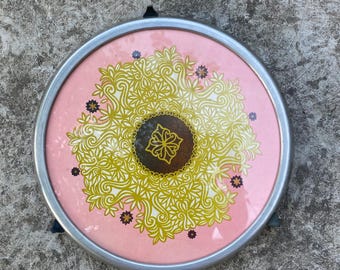 Op de afbeelding: Een ronde, roze dienblad met een zilveren metalen frame. Het dienblad heeft een gouden en bruin mandala-ontwerp met ingewikkelde details.