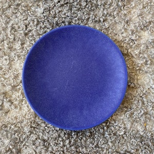 May include: A solid blue ceramic plate on a fluffy white faux fur background.