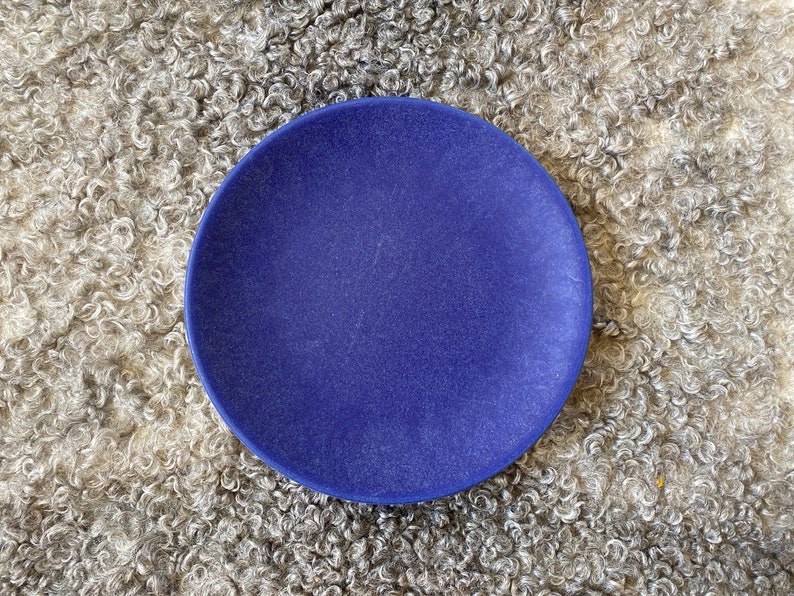 May include: A solid blue ceramic plate on a fluffy white faux fur background.
