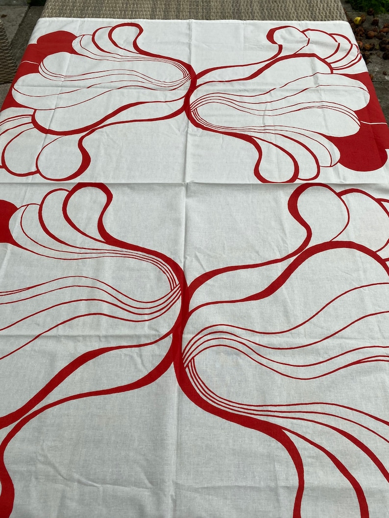 May include: White fabric with a red abstract design of overlapping curved lines and shapes. The design is symmetrical and appears twice on the fabric.