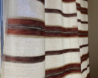 Puede incluir: Primer plano de cortinas a rayas. Las cortinas presentan rayas horizontales alternas en blanco roto y varios tonos de marrón. La tela tiene una textura tejida y las cortinas cuelgan frente a una ventana.