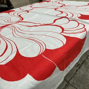 May include: White tablecloth with a red abstract floral pattern. The tablecloth is made of a soft, woven fabric and features a repeating design of stylized flowers.