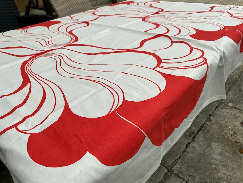 May include: White tablecloth with a red abstract floral pattern. The tablecloth is made of a soft, woven fabric and features a repeating design of stylized flowers.