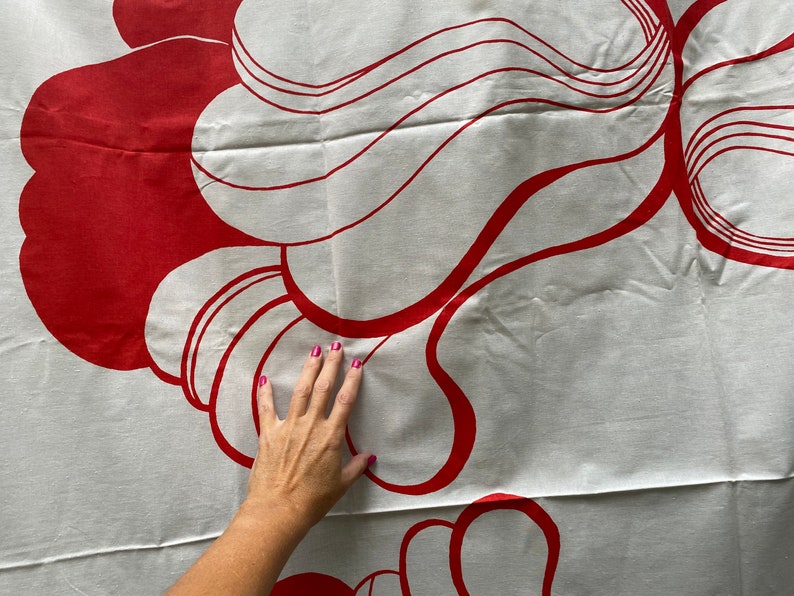 May include: White fabric with a red abstract design. The design features a series of overlapping, curved shapes.
