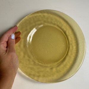 May include: A yellow glass plate with a textured surface. The plate has a raised rim and a slightly indented center.
