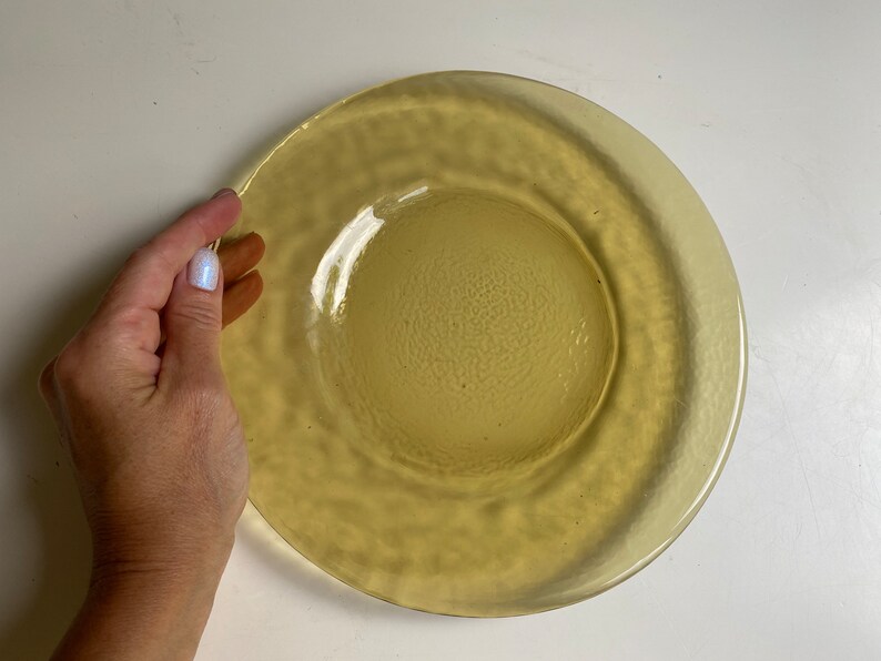 May include: A yellow glass plate with a textured surface. The plate has a raised rim and a slightly indented center.