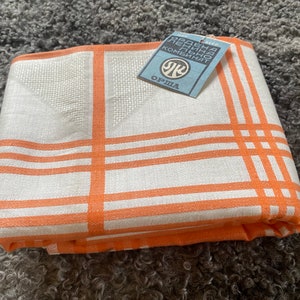 Puede incluir: Un mantel blanco con rayas naranjas y un pequeño diseño bordado en el centro. El mantel está doblado y tiene una etiqueta adjunta que dice "Орша" y "РАДЫЕНА ЛЕНИНА ПРЯДИЛЬНЫЙ КОМБИНАТ".