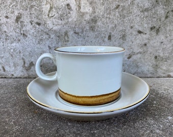 May include: A white ceramic coffee cup with a brown band around the top. The cup is sitting on a matching saucer.