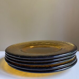 May include: Four amber glass dinner plates stacked on top of each other. The plates have a textured, rippled surface.