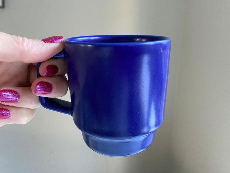 May include: A blue ceramic mug with a rounded shape and a handle. The mug is made of a smooth, glossy material.