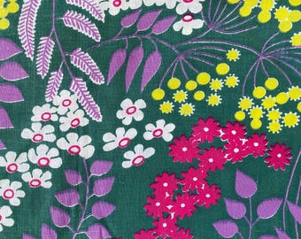 May include: A green fabric with a floral pattern. The pattern features white, pink, and yellow flowers with purple leaves.