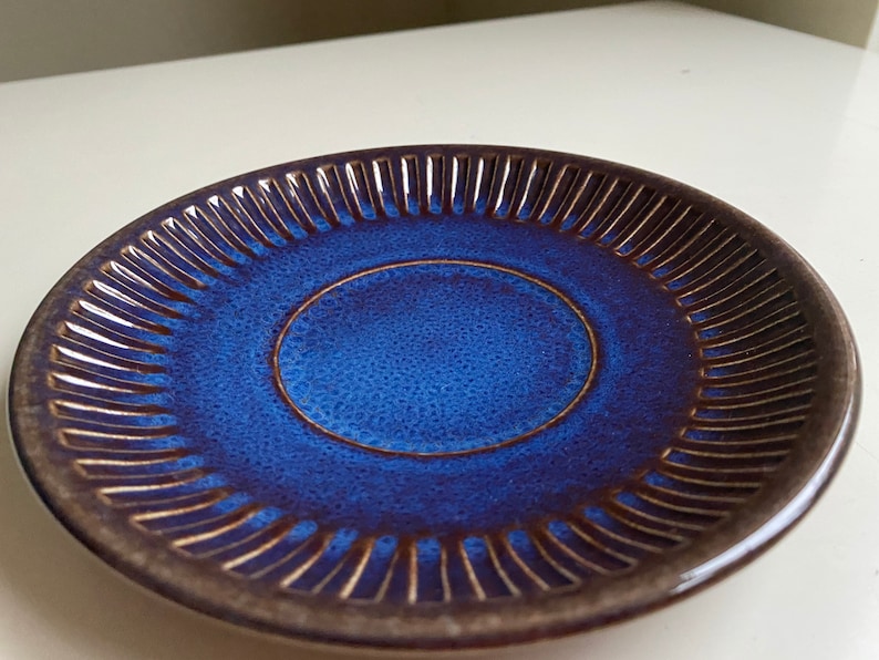 Puede incluir: Un platillo de cer&aacute;mica azul con un borde marr&oacute;n y un dise&ntilde;o elevado y texturizado alrededor del borde.