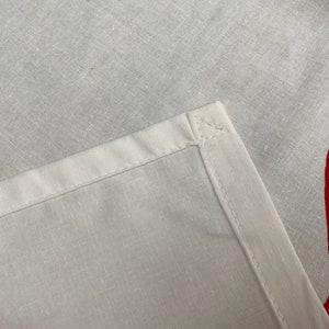 May include: Close-up of a white fabric with a red design. The fabric has a seam along the edge.