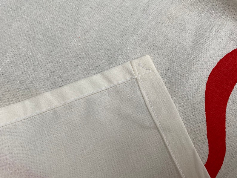May include: Close-up of a white fabric with a red design. The fabric has a seam along the edge.