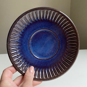 Puede incluir: Un platillo de cer&aacute;mica azul con un borde marr&oacute;n oscuro y un dise&ntilde;o texturizado y acanalado. El platillo tiene un esmalte azul oscuro.