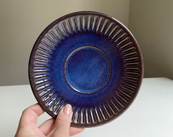 May include: A blue ceramic saucer with a dark brown rim and a textured, ribbed design. The saucer has a deep blue glaze.