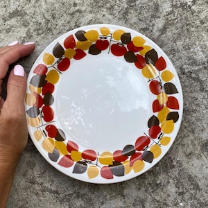 May include: A white ceramic plate with a brown, red, and yellow leaf design around the rim.