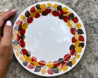 May include: A white ceramic plate with a brown, red and yellow leaf design around the rim.