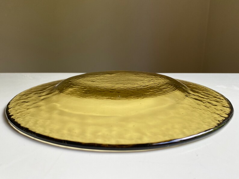 May include: A brown glass plate with a textured surface. The plate is round and has a slightly raised edge.