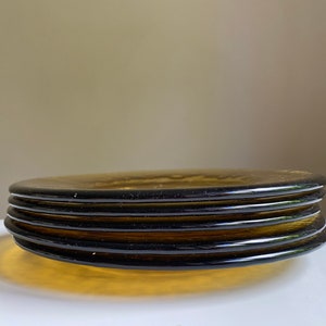 May include: A stack of four amber glass plates with a dark brown rim. The plates are stacked on a white surface.