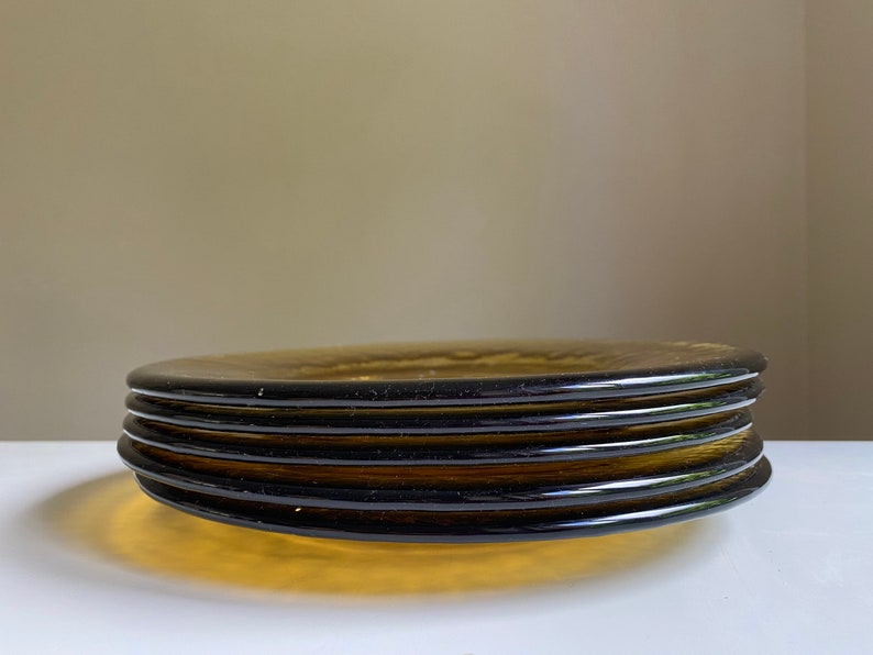 May include: A stack of four amber glass plates with a dark brown rim. The plates are stacked on a white surface.
