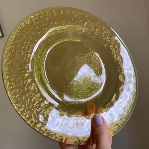 May include: A yellow glass plate with a textured surface. The plate has a raised rim and a slightly indented center.