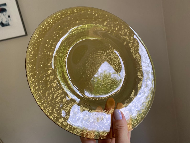 May include: A yellow glass plate with a textured surface. The plate has a raised rim and a slightly indented center.