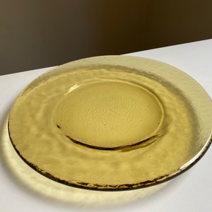 May include: A large, amber-colored glass plate with a textured surface. The plate has a slightly raised rim and a smooth, circular center.