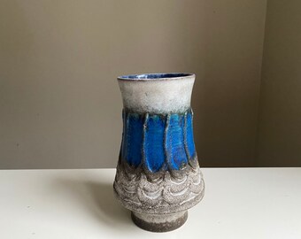 May include: A white and blue ceramic vase with a textured, wavy design. The vase has a wide base and a narrow neck.