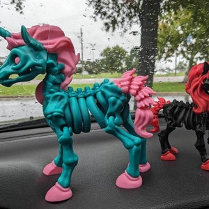 Könnte beinhalten: Zwei Skelett-Einhorn-Figuren, eine türkis mit rosa Mähne und Schwanz, die andere schwarz mit roter Mähne und Schwanz.