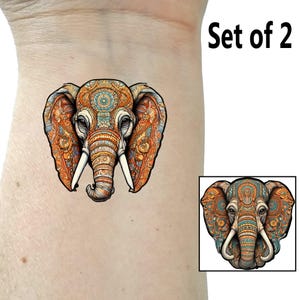 May include: Set of two temporary tattoos featuring a colorful, detailed elephant head with intricate patterns. The elephant has large, white tusks and a blue, orange, and yellow color scheme.