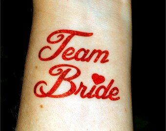 May include: Red glitter temporary tattoo that says "Team Bride" with a small red heart.