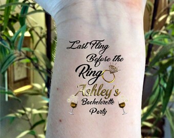 May include: A temporary tattoo with the text "Last Fling Before the Ring Ashley's Bachelorette Party" and a gold ring with a diamond. Two wine glasses with bubbles are on either side of the text.