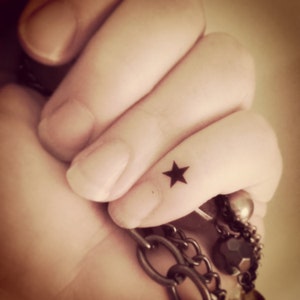 May include: A close-up of a finger with a small black star tattoo.