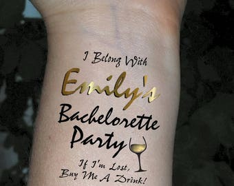 May include: A temporary tattoo with gold lettering that says "I Belong With Emily's Bachelorette Party" and a glass of wine with the text "If I'm Lost, Buy Me A Drink!"