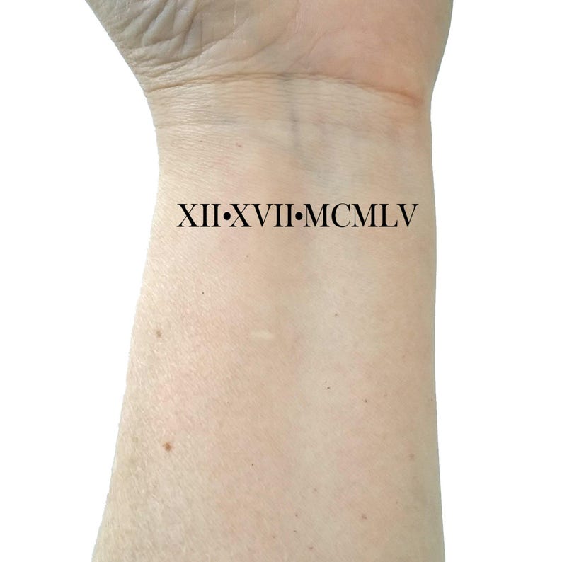 May include: A close-up of a person's wrist with a black tattoo that reads "XII.XVII.MCMLV".