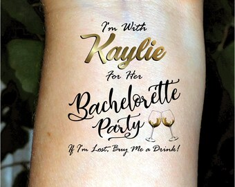 May include: A temporary tattoo with gold lettering that reads "I'm With Kaylie For Her Bachelorette Party" with two champagne glasses clinking. The text "If I'm Lost, Buy Me a Drink!" is below the glasses.