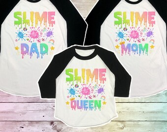 May include: Three white baseball shirts with black sleeves. The shirts have a rainbow slime design with the words "Slime Dad", "Slime Mom", and "Slime Queen".