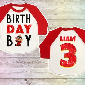 May include: Red and white baseball style shirt with a distressed graphic of a cartoon baby and the text "BIRTHDAY BOY". The back of the shirt has a red number "3" with a yellow outline and the name "LIAM" above it.