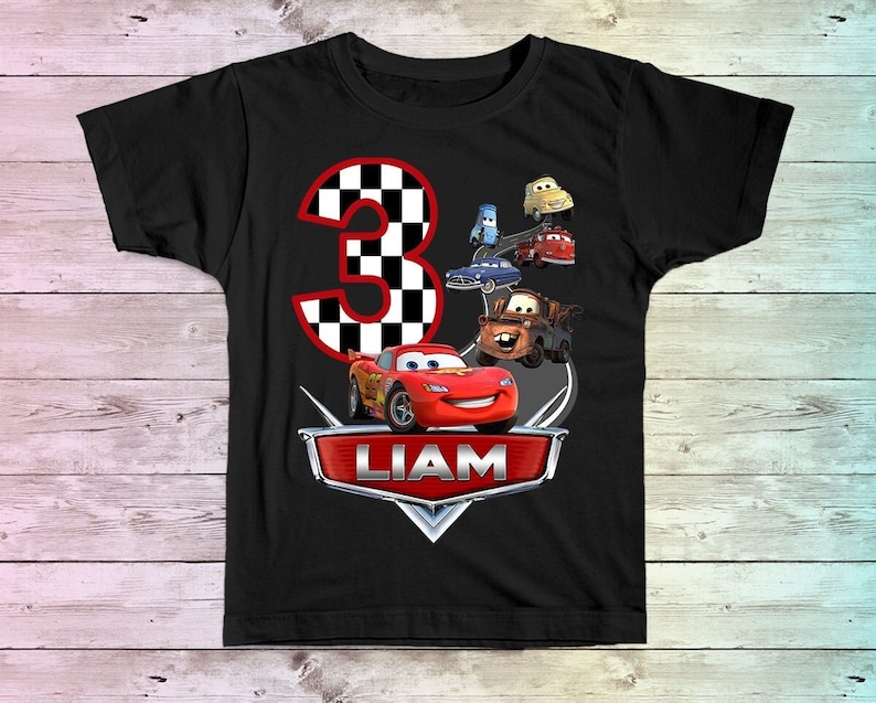 May include: Black t-shirt with a red and black checkered number 3, a red race car, and other cartoon cars. The text "LIAM" is on the shirt.